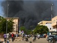 People watch as black smoke rises as the capital of Burkina Faso came under multiple attacks on March 2, 2018, targeting the French embassy, the French cultural centre and the country's military headquarters. Witnesses said five armed men got out of a car and opened fire on passersby before heading towards the embassy, in the centre of the city. Other witnesses said there was an explosion near the headquarters of the Burkinabe armed forces and the French cultural centre, which are located about a kilometre (half a mile) from the site of the first attack.