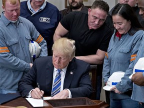 U.S. President Donald Trump signs a proclamation on adjusting imports of steel into the United States next to steel and aluminum workers at the White House on Thursday, March 8, 2018.