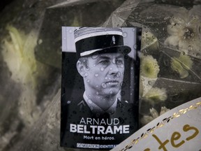 A photo of Lieutenant Colonel Arnaud Beltrame placed on a bunch of flowers at the main gate of the Police headquarters in Carcassonne, France, Saturday, March 24, 2018, following an attack on a supermarket in Trebes in the south of the country on Friday. A French police officer who offered himself up to an Islamic extremist gunman in exchange for a hostage died of his injuries, raising the death toll in the attack to four, and the officer was honored Saturday as a national hero of "exceptional courage and selflessness."