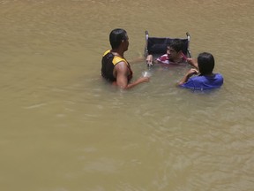 In this March 11, 2018 photo, a Venezuelan family, one in a wheelchair, cool off and bathe in the Branco River in Boa Vista, Roraima state, Brazil. Some Venezuelans arrive to Brazil wearing baggy clothes, have emaciated faces and complain of medical issues ranging from children with measles to diabetics with no insulin.