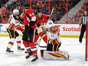 Goaltender David Rittich of the Calgary Flames has the puck bounce off his facemask while having to contend with Ottawa Senators' Jean-Gabriel Pageau, left, and Mark Stone during NHL action Friday in Ottawa. Rittich had 29 saves in a 2-1 Flames victory.