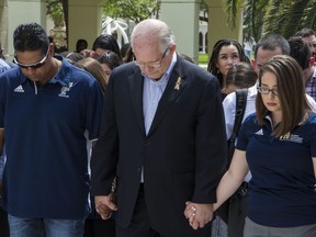 Florida International University President Mark B. Rosenberg, center, joins hands with baseball coach Mervyl Melendez, left, and student government president Krista Schmidt, as they bow their heads during a moment of silence for the victims of the bridge collapse at the school four days earlier, Monday, March 19, 2018, in Miami.