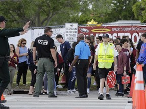 Students wait to cross the street after their first day back at Marjory Stoneman Douglas High School in Parkland, Fla., Wednesday, Feb. 28, 2018.  The students were greeted Wednesday morning by police officers carrying military style rifles and an array of counselors and therapy dogs. They missed two weeks of school following the Feb. 14 mass shooting that killed several students and teachers.