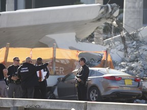 Police work next to a crushed car under a section of a collapsed pedestrian bridge, Friday, March 16, 2018 near Florida International University in the Miami area.   The new pedestrian bridge that was under construction collapsed onto a busy Miami highway Thursday afternoon, crushing vehicles beneath massive slabs of concrete and steel, killing and injuring several people, authorities said.