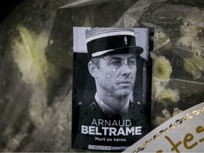 A photo of Lieutenant Colonel Arnaud Beltrame placed on a bunch of flowers at the main gate of the Police headquarters in Carcassonne, France, Saturday, March 24, 2018, following an attack on a supermarket in Trebes in the south of the country on Friday. A French police officer who offered himself up to an Islamic extremist gunman in exchange for a hostage died of his injuries, raising the death toll in the attack to four, and the officer was honored Saturday as a national hero of "exceptional courage and selflessness."