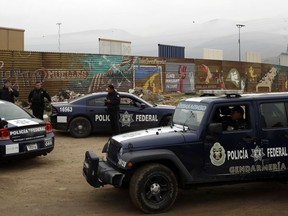 Mexican federal police officers stand guard on the Mexico side of the border on Tuesday, March 13, 2018, in Tijuana, Mexico. President Trump is scheduled to visit the site of the border wall prototypes which can be seen in the background behind the wall.