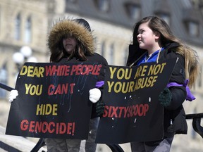 Skylar S., 15, and her sister Aponi, 12, right, whose mother is a Sixties Scoop survivor, hold signs during a national solidarity rally called by the National Indigenous Survivors of Child Welfare Network on Parliament Hill in Ottawa on Friday, March 16, 2018.