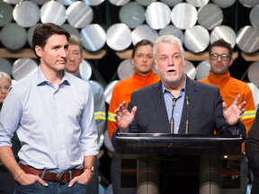 Prime Minister Justin Trudeau, left, looks on as Quebec Premier Philippe Couillard speaks to workers and reporters at a news conference during a visit of the Rio Tinto aluminum plant on March 12, 2018 in Saguenay Que.