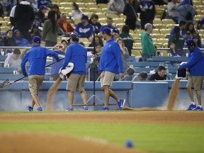 Members of the grounds crew pour dirt near third base after a water pipe broke during the fifth inning of an exhibition baseball game between the Los Angeles Dodgers and the Los Angeles Angels, Tuesday, March 27, 2018, in Los Angeles.