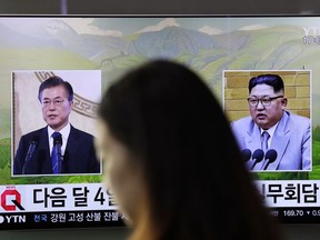 A visitor walks by a TV screen showing file footages of South Korean President Moon Jae-in, left, and North Korean leader Kim Jong Un, right, during a news program at the Seoul Railway Station in Seoul, South Korea, Thursday, March 29, 2018. North Korean leader Kim will meet South Korean President Moon at a border village on April 27, the South announced Thursday after the nations agreed on a rare summit that could prove significant in global efforts to resolve a decades-long standoff over the North's nuclear program.