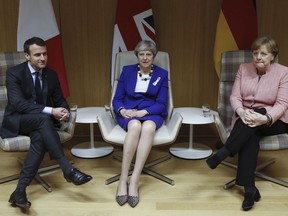 Britain's Prime Minister Theresa May, centre, is flanked by French President Emmanuel Macron and German Chancellor Angela Merkel, before their trilateral meeting at the European Union leaders summit in Brussels, Belgium, Thursday March 22, 2018.  British Prime Minister Theresa May won the backing of 27 other European Union leaders on Thursday in blaming Russia for the poisoning of a former spy on English soil.