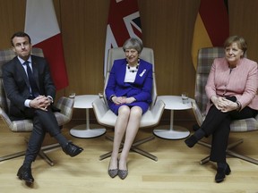 Britain's Prime Minister Theresa May, centre, is flanked by French President Emmanuel Macron and German Chancellor Angela Merkel, before their trilateral meeting at the European Union leaders summit in Brussels, Belgium, Thursday March 22, 2018.  Theresa May won the backing of 27 other European Union leaders on Thursday in blaming Russia for the poisoning of a former spy on English soil.