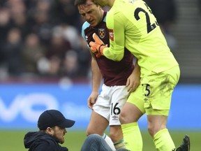 A Pitch invader falls to the pitch confronted by West Ham's Mark Noble, with goalkeeper Joe Hart, right, during the English Premier League soccer match between Burnley and West Ham at the Olympic London Stadium in London, Saturday, March 10, 2018.