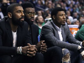 Boston Celtics guard Kyrie Irving, left, sit with teammates Jaylen Brown, center, and Marcus Smart during the first quarter of the team's NBA basketball game against the Oklahoma City Thunder in Boston, Tuesday, March 20, 2018. All three starters are sidelined with injuries.