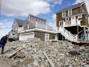 A passerby pauses near a pile of rocks, sand and debris near beachfront homes, Sunday, March 11, 2018, in Marshfield, Mass. The Northeast is bracing for its third nor'easter in fewer than two weeks. The National Weather Service reports Sunday that a southern storm is expected to make its way up the coast causing more snowfall.