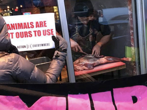 Chef Michael Hunter carves up a deer leg in the window of Toronto's Antler restaurant as  animal rights activists protest outside.