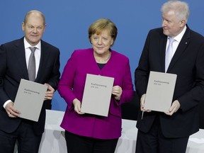 From left, Olaf Scholz, acting chairman of the German Social Democratic Party (SPD), German Chancellor and chairwomen of the German Christian Democratic Union (CDU), Angela Merkel, and the chairman of the German Christian Social Union (CSU), Horst Seehofer, pose with the coalition agreement during a signing ceremony in Berlin, Germany, Monday, March 12, 2018.