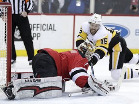 New Jersey Devils goaltender Keith Kinkai, front, reaches for the puck next to Pittsburgh Penguins center Riley Sheahan (15) during the first period of an NHL hockey game Thursday, March 29, 2018, in Newark, N.J.