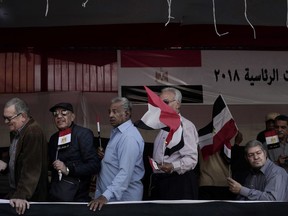 Egyptian men wave national flags as they wait in line to vote during the first day of the presidential election in front of a polling site in Cairo, Egypt, Monday, March 26, 2018.  Egyptians head to the polls on Monday but the presidential election this time is not about who wins -- that was settled long ago -- but about how many people bother to cast ballots.