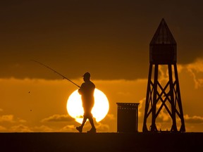 FILE - In this July 14, 2016, file photo, a fisherman prepares to cast a line as the sun rises behind him as he fishes off a jetty into the Atlantic Ocean, in Bal Harbour, Fla. Florida will join most of the nation Sunday, March 11, 2018, in springing ahead, moving clocks up one hour to observe daylight saving time.