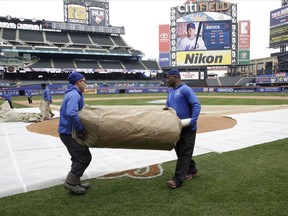 Workers prepare to lay a tarp out to protect the field during batting practice before a New York Mets workout, Wednesday, March 28, 2018, in New York. The team's opening day is Thursday against the St Louis Cardinals.