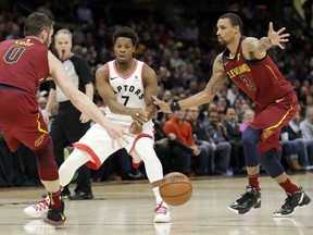 Toronto Raptors guard Kyle Lowry passes the ball between the Cavaliers' Kevin Love, left, and George Hill during the first half of their game Wednesday night in Cleveland.