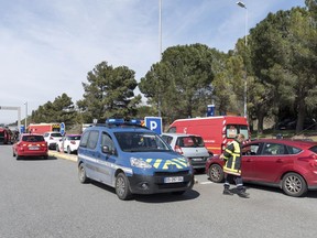 French police and firefighters secure the entrance of Trebes, southern France, where an armed man took hostages in a supermarket, Friday, March 23, 2018. French national police say two people have been killed and about a dozen wounded in a shooting and hostage-taking in a super market in southern France.