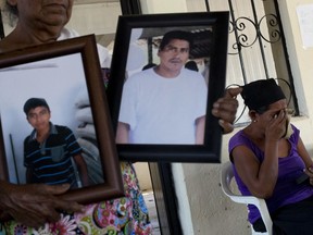 In this Feb. 5, 2018 photo, Demetria Calixto Gaspare, 58, right, cries as she looks at a picture of her son Jesus Estrada Calixto, 26, who was killed in January allegedly by "community police", along with five other civilians, including Sofia Leon Estrada's son Alejandro Melchor Leon, 47, pictured center, and grandson, Alejandro Melchor Angel, 16, pictured left, as family members visit the town council building, in La Concepcion, Mexico.