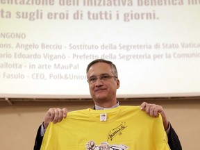 FILE - In this Feb. 8, 2018 file photo, Vatican's Secretariat of Communication Mons. Dario Vigano' holds a jersey bearing a reproduction of the graffitti of the SuperPope by artist Maupal, Mauro Pallotta, sitting at left, during the presentation of a charity campaign "Ordinary Heroes" at the Vatican. On Wednesday, March 21, 2018, the Vatican announced that Vigano' had resigned over a scandal about a letter from the retired pope that he mischaracterized in public and then had digitally manipulated in a photograph sent to the media.