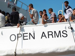 In this July 13, 2017 photo, migrants stand on the deck of the Spanish NGO's Proactiva Open Arms vessel at harbor at Porto Empedocle in the southern Italian island of Sicily. The Italian news agency ANSA says the NGO's migrant rescue ship has been put under sequester by prosecutors' orders, Sunday, March 18, 2018, in Pozzallo port, Sicily, where, a day earlier, the vessel brought 216 migrants it had rescued last week in the Mediterranean north of Libya.