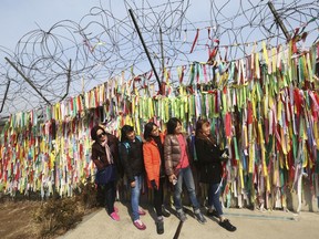 Visitors pose in front of ribbons placed on a barbed wire fence with messages wishing for the reunification of the two Koreas at the Imjingak Pavilion in Paju, near the border with North Korea, South Korea, Wednesday, March 7, 2018. The meeting between North Korean leader Kim Jong Un and South Korean envoys marked the first time South Korean officials have met with the young North Korean leader in person since he took power after his dictator father's death in late 2011. It's the latest sign that the Koreas are trying to mend ties after one of the tensest years in a region that seems to be permanently on edge.