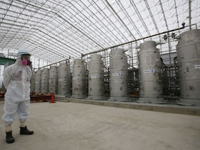 FILE - In this Nov. 12, 2014, file photo, a Tokyo Electric Power Co. (TEPCO) official wearing a radioactive protective gear stands in front of Advanced Liquid Processing Systems during a press tour at the Fukushima Dai-ichi nuclear power plant in Okuma, Fukushima Prefecture, northeastern Japan. A government-commissioned group of experts concluded Wednesday, March 7, 2018 that a costly underground ice wall is only partially effective in reducing the ever-growing amount of contaminated water at the destroyed Fukushima nuclear plant, and that other measures are needed as well.