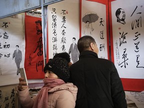 In this March 1, 2018, photo, a women takes a picture as a couple looks at posters featuring drawings of Chinese President Xi Jinping and late communist leader Mao Zedong with their quotes, on display for sale at a market in Beijing. Many Western scholars who studied China believed that the opening to the outside world engineered by reformer Deng Xiaoping in the early 1980s would pave the way for corresponding political freedoms. That vision has been categorically shattered under President Xi Jinping, who many once thought would be the next great reformer. In just five years, Xi has consolidated more power than any Chinese leader since Mao Zedong and is now primed to rule as president-for-life.