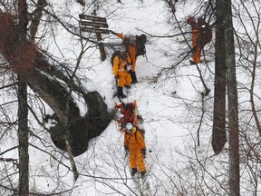 Rescuers walk near the site where holiday hikers were found in Hinohara village, Tokyo's Okutama region, Thursday, March 22, 2018. Thirteen hikers, reportedly including Chinese citizens, were rescued after getting trapped overnight on a snowy Tokyo mountain trail. They spent the night on one of the mountains in Tokyo's popular hiking area. Tokyo police and disaster officials said Thursday that seven of them who couldn't walk were airlifted. Six others hiked down escorted by rescue workers.