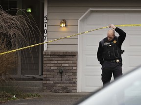 A Pierce County Sheriff's Dept. deputy walks under crime scene tape, Tuesday, March 13, 2018, in front of a home in Spanaway, Wash., where authorities say a member of the U.S. Air Force, who was stationed at Joint Base Lewis-McChord, fatally shot his two young children and their mother before killing himself overnight.