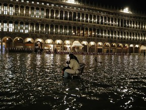 People sit in a flooded St. Mark's Square in Venice, Italy, Friday, March 30, 2018. High tides flooded Venice, leading Venetians and tourists to don high boots and use wooden walkways to cross the square and other areas under water.