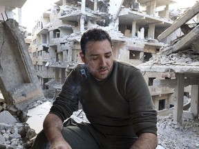This Monday, March. 26, 2018 photo provided by Danny Makki, a British-born Syrian journalist, which has been verified and is consistent with other AP reporting, shows him smoking near damaged buildings due to fighting and Syrian government airstrikes in the town of Harasta, in eastern Ghouta region east of Damascus, Syria. A journey that before the war was just a 15-minute drive from Damascus now took well over an hour, clambering over giant ramparts of dirt and rubble. Visiting his house for the first time in six years in the town of Harasta, Danny Makki couldn't recognize it. (Danny Makki via AP)