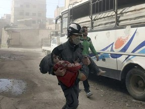 This photo provided by the Syrian Civil Defense White Helmets, which has been authenticated based on its contents and other AP reporting, shows a member of the Syrian Civil Defense group carrying a boy who was wounded during airstrikes and shelling by Syrian government forces in Ghouta, a suburb of Damascus, Syria, Friday, March. 2, 2018. The Russia-ordered pause came after a U.N. Security Council resolution calling for a nationwide 30-day cease-fire failed to take hold. While the relentless bombing has somewhat subsided in eastern Ghouta, home to around 400,000 civilians, the Syrian government's push to squeeze the insurgents out of the region continued. (Syrian Civil Defense White Helmets via AP)