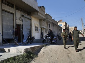 Members of the Kurdish internal security forces, right, pass next of damaged shops, at the scene where an explosion on Thursday hit a U.S.-led coalition vehicles, killing an American and a Briton soldiers, in Manbij town, north Syria, Saturday, March 31, 2018. The explosion on Thursday was the first to hit members of the U.S.-led coalition who have deployed to Manbij months after the town was liberated from Islamic State militants in 2016. An improvised explosive device went off during an operation against a known member of the Islamic State group in this mixed Arab and Kurdish town, the U.S-led Coalition said in a statement Saturday.