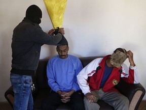A Kurdish security officer takes off face masks from Alexanda Amon Kotey, left, and El Shafee Elsheikh, who were allegedly among four British jihadis who made up a brutal Islamic State cell dubbed "The Beatles," for an interview with The Associated Press at a security center in Kobani, Syria, Friday, March 30, 2018.