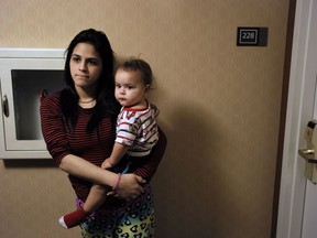 In this Tuesday, Feb. 27, 2018 photo, Jesenia Flores holds her son Jose, both of Aibonito, Puerto Rico, as they wait to enter her mother-in-law's hotel room, in Dedham, Mass. Nearly six months after Hurricane Maria, thousands of Puerto Ricans are still staying in hotels. It's frustrating "to be cooped up here without knowing what will happen to us," the 19-year-old mother said.