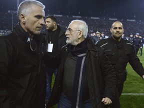 In this photo taken on Sunday, March 11, 2018, PAOK owner, businessman Ivan Savvidis, center, escorted by his bodyguards leaves the pitch during a Greek League soccer match between PAOK and AEK Athens in the northern Greek city of Thessaloniki. A disputed goal at the end of the Greek league match led to a pitch invasion by Savvidis, who appeared to be carrying a gun. (AP Photo)