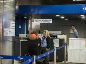 In this Wednesday, Feb. 21, 2018 photo, a woman delivers her luggage to a security officer, at the airport of the northern Greek city of Thessaloniki. Last year, Greek police caught a total of 1,672 migrants trying to sneak out of Greece by plane. There's a thriving illegal industry in Greece that churns out counterfeit passports and identity papers.