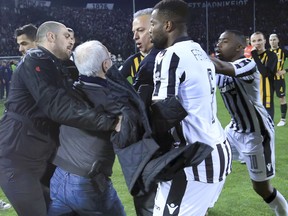 PAOK owner, businessman Ivan Savvidis, second from left, approaches AEK Athens' Manager Operation Department Vassilis Dimitriadis, center, as his bodyguard and PAOK's players Fernando Varela, second from right, and Djalma Campos, right, try to stop him during a Greek League soccer match between PAOK and AEK Athens in the northern Greek city of Thessaloniki, Sunday, March 11, 2018. A disputed goal at the end of the Greek league match led to a pitch invasion by Savvidis, who appeared to be carrying a gun. Savvidis came on the field twice. It's unclear this photos shows his first time or second.