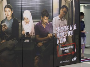 A commuter walks past an advertisement discouraging the dissemination of fake news at a train station in Kuala Lumpur, Malaysia, Thursday, March 29, 2018. Malaysia's government has cut the proposed punishment for fake news offenders from 10 to six years in prison following an outcry from rights groups and opposition lawmakers who say the bill aims to silence dissent ahead of a general election.