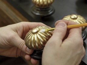 A craftsman uses a small artists brush to press the gold leafing material into the detailed carved elements of the finial on a Georgetown bed.