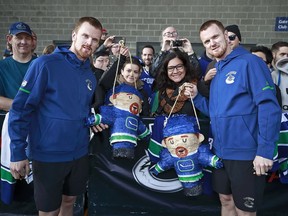 Daniel Sedin (left) and Henrik Sedin hold Sedin piñatas as they pose with a fans during a team autograph signing before a game against the Columbus Blue Jackets on March 31.