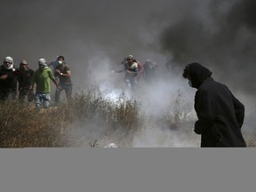 Palestinian protesters run to cover from teargas fired by Israeli troops after they burn tires near the fence during a protest at the Gaza Strip's border with Israel, east of Khan Younis, Friday, April 27, 2018. Palestinians converged on the Gaza border with Israel for a fifth round of weekly protests Friday, some throwing stones and burning tires, as a top U.N. official urged Israel to refrain from using excessive force against them.