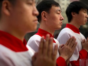 FILE - In this Saturday, March 31, 2018, file photo, Chinese acolytes pray during a Holy Saturday Mass on the evening before Easter at the Cathedral of the Immaculate Conception, a government-sanctioned Catholic church in Beijing. China says restricting the Vatican's control over the appointment of bishops does not infringe upon Chinese believers' religious freedom. The remark during a State Council briefing comes as Beijing and the Holy See are negotiating an historic agreement over the method of selecting bishops in China.