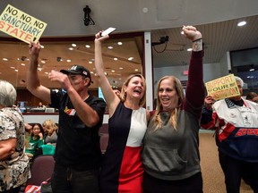 FILE - In this March 27, 2018, file photo, David Hernandez, left, Genevieve Peters, center, and Jennifer Martinez celebrate after the Orange County Board of Supervisors voted to join the U.S. Department of Justice lawsuit against the State of California's sanctuary cities law (SB54) during their meeting in Santa Ana, Calif. More local governments in California are resisting the state's efforts to resist the Trump administration's immigration crackdown, and political experts see politics at play as Republicans try to fire up voters in a state where the GOP has grown weak.